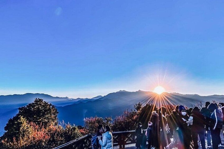 A sunset over a mountainous landscape with people standing on a viewing platform. 2