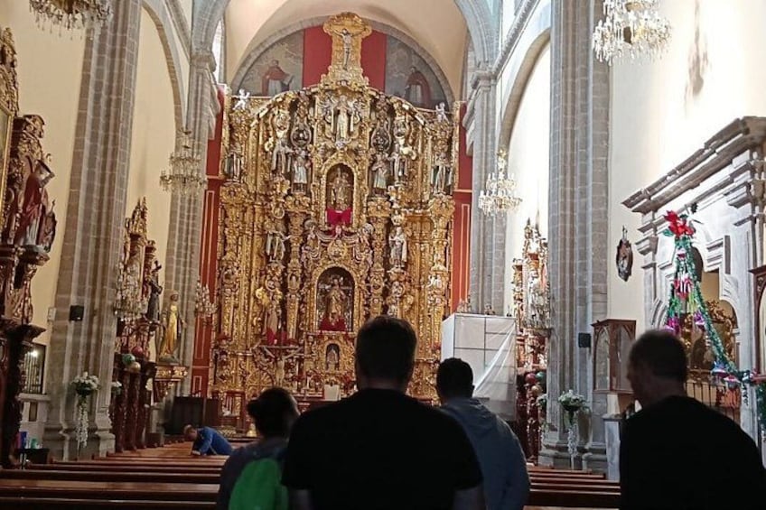 An ornate church interior with a large altar, religious statues, and chandeliers. 3