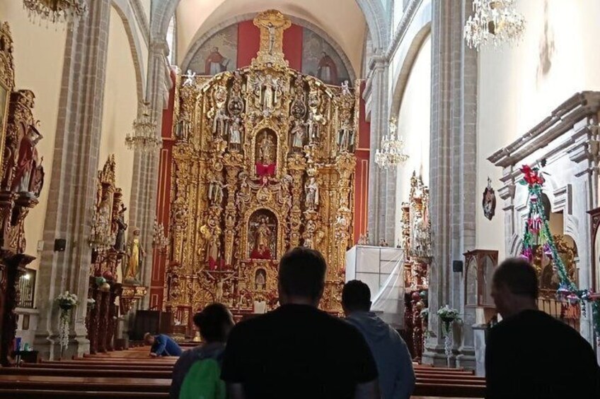 An ornate church interior with a central altar, pews, and chandeliers. 3