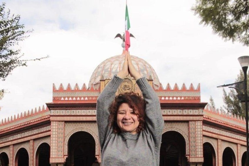 A person holding a flag with a green field and red stripes, standing in front of a building with a dome and arched windows. 1