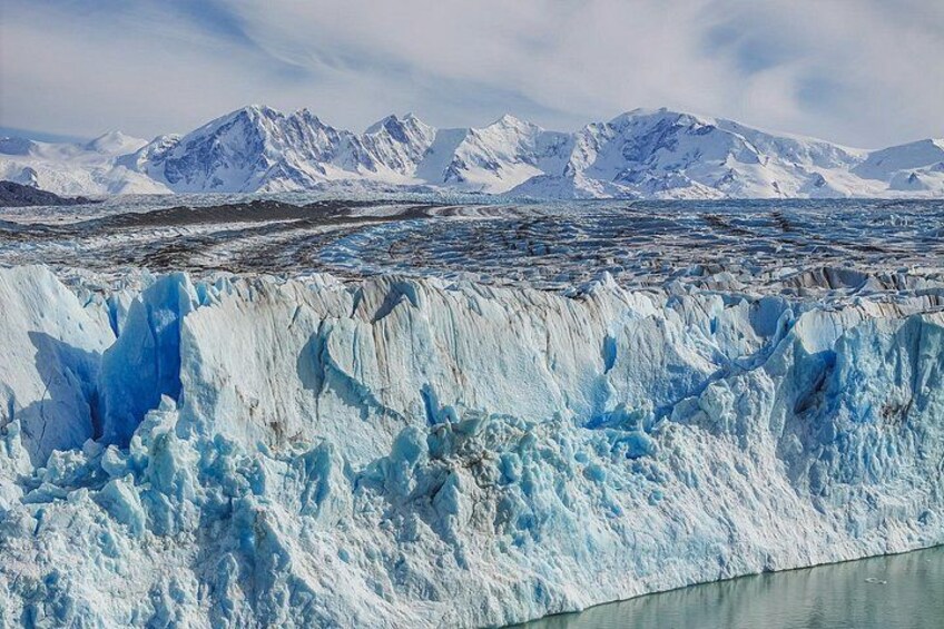 A glacier with a blue hue, mountains in the background, and a clear sky. 5