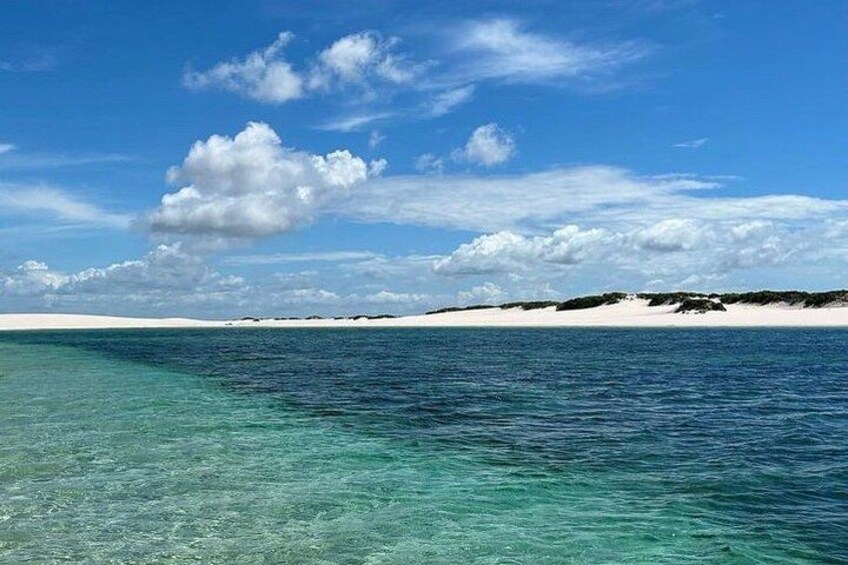 A clear blue sea with a sandy beach and a distant landmass under a partly cloudy sky. 3