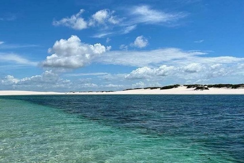 Mar azul transparente con una playa de arena y una tierra a lo lejos. 2