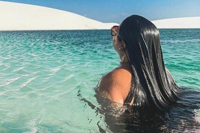 Una persona de cabello largo en aguas turquesas cristalinas, con una playa de arena blanca y un cielo despejado al fondo. 2