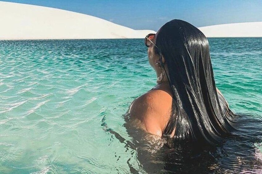 A person in clear turquoise water with white sand dunes in the background. 1