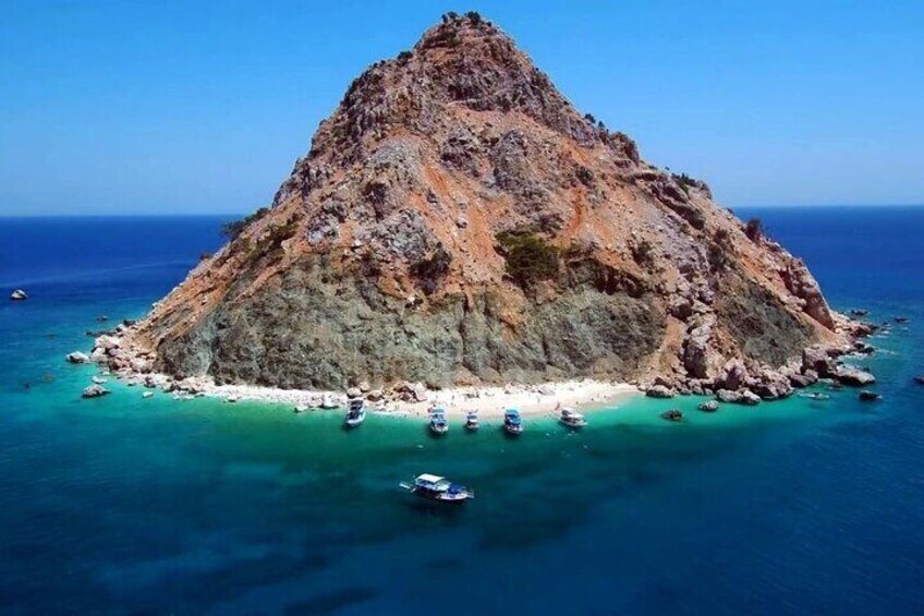 A rocky island surrounded by turquoise waters with several boats anchored near the shore. 3