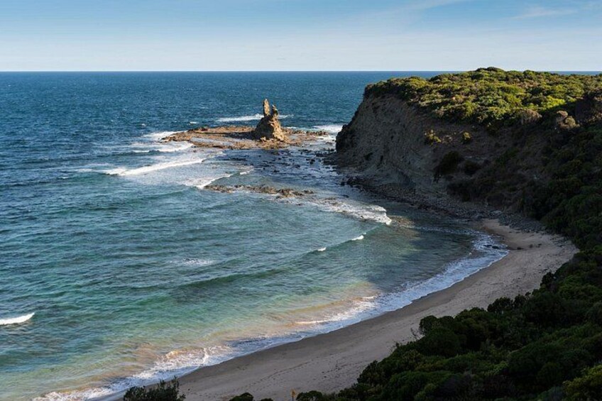 A coastal landscape with a rocky outcrop, a sandy beach, and a cliff with vegetation. 4