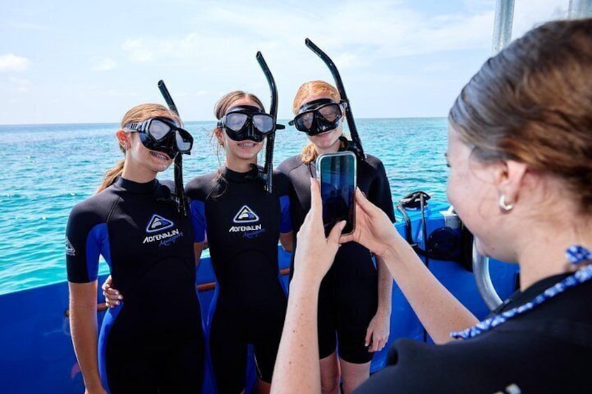 Tre persone in mute nere con attrezzatura da immersione, in piedi su una barca con l'oceano sullo sfondo. 5