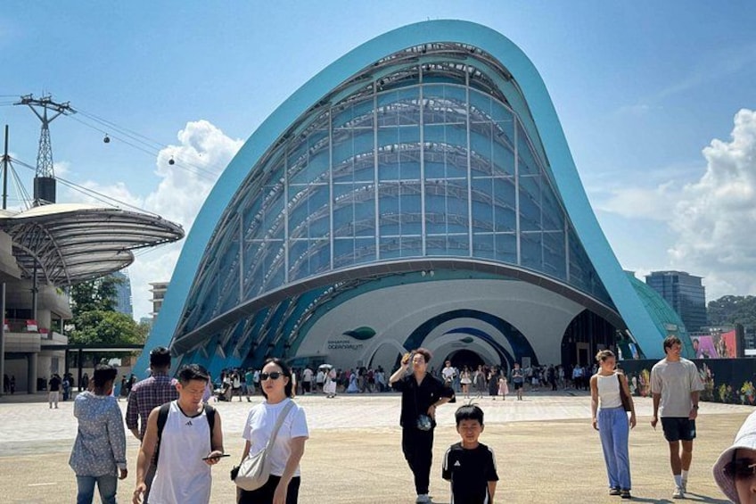 A modern architectural building with a curved glass facade, surrounded by a crowd of people. 2
