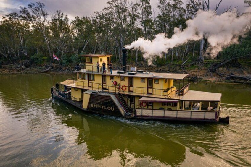 A yellow riverboat named 'EMMYLOU' with a cabin and a staircase, floating on a river with trees and smoke in the background. 2