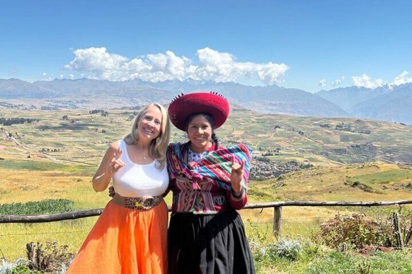 Two people standing on a hill with a mountainous landscape in the background. 1