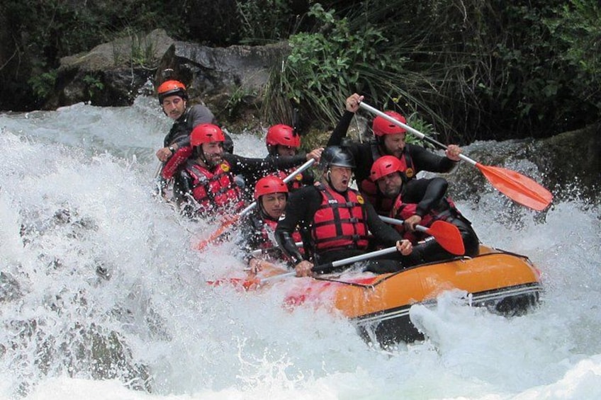 A group of people in an orange raft navigating through a river with white water rapids. 1