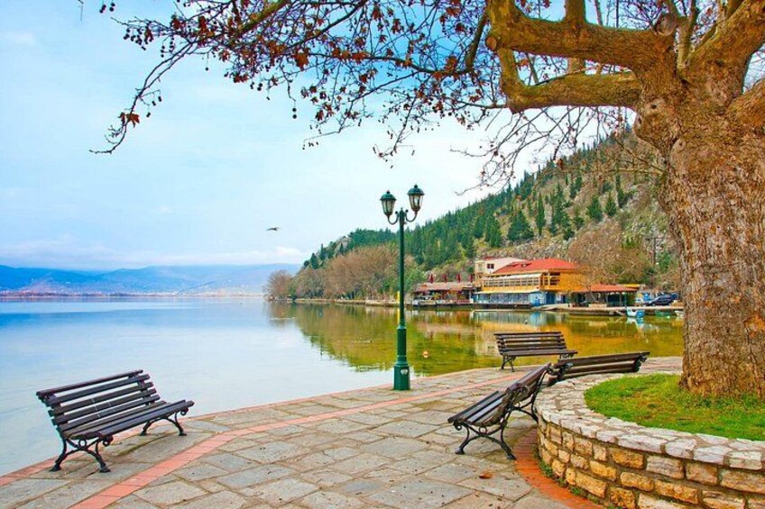 A lakeside park with benches, a lamp post, and a boat on the water. 2