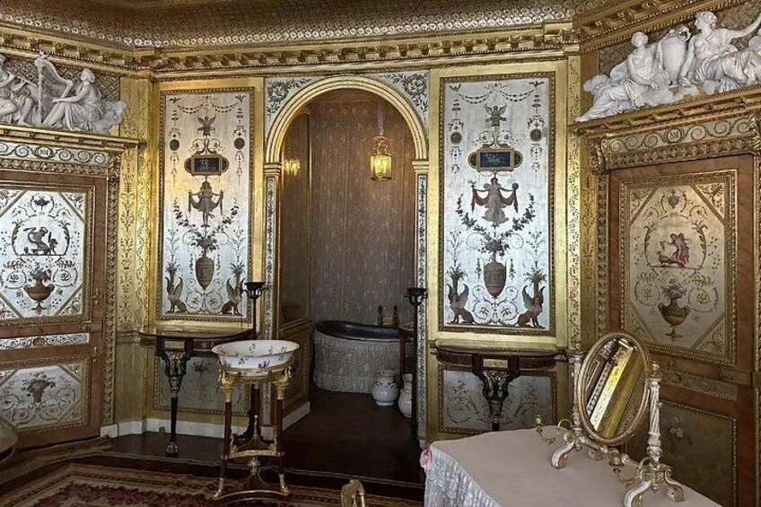 An opulent room with ornate gold decorations, a large mirror, and a detailed mural on the wall. 3