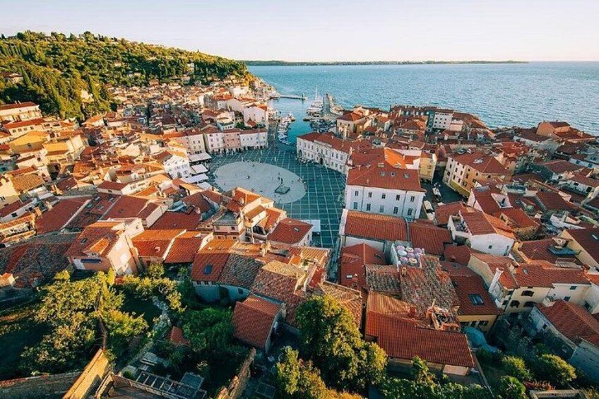 A coastal town with red-roofed buildings, a central square, and a body of water. 1