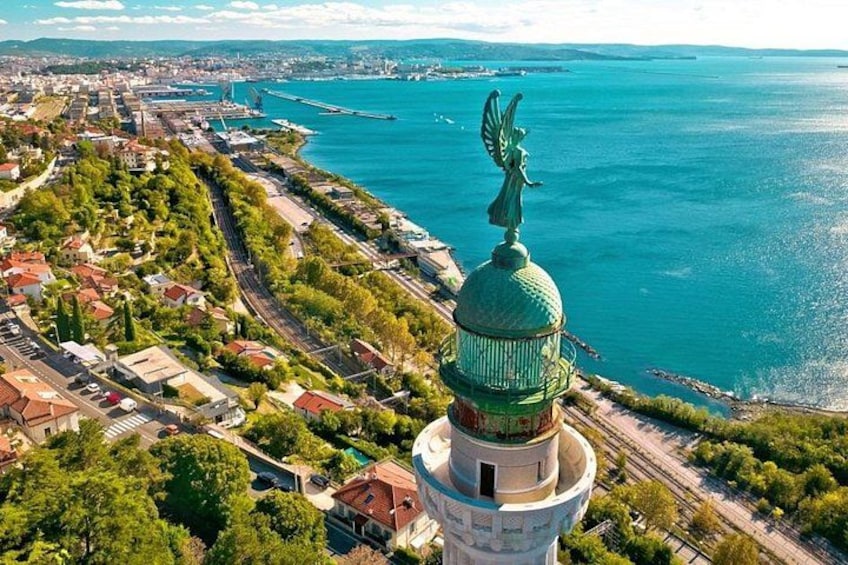 A coastal cityscape with a prominent lighthouse and a statue on top, surrounded by greenery and residential buildings. 3