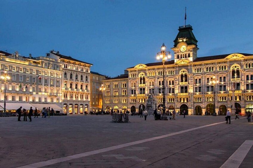 A historic building with a clock tower, surrounded by a square with people walking. 2