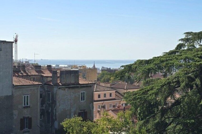 A coastal cityscape with terracotta-roofed buildings, a clear sky, and a view of the sea. 5