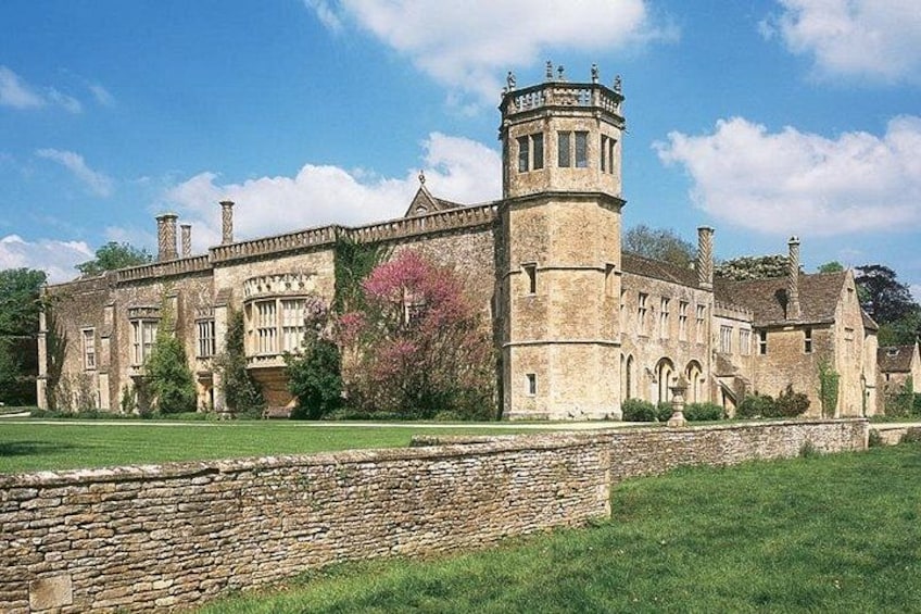 A historic stone building with a tower, surrounded by a well-maintained lawn and a stone wall. 2