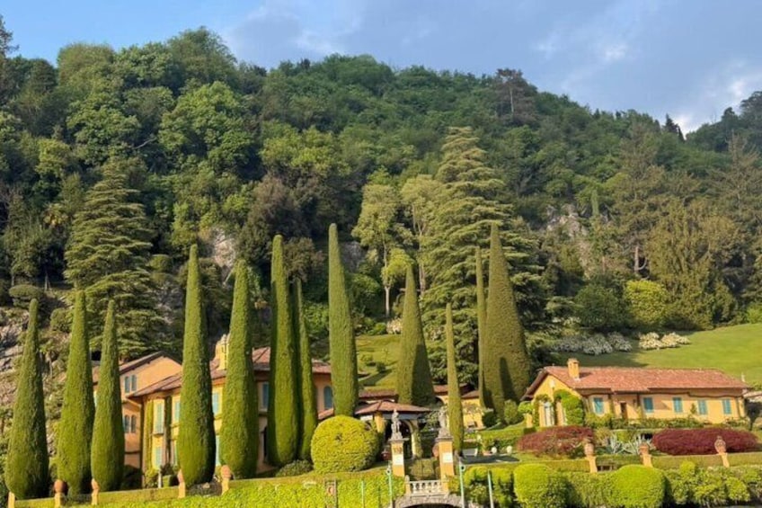 A landscaped garden with neatly trimmed hedges, a row of tall cypress trees, and a building with a red roof. 4