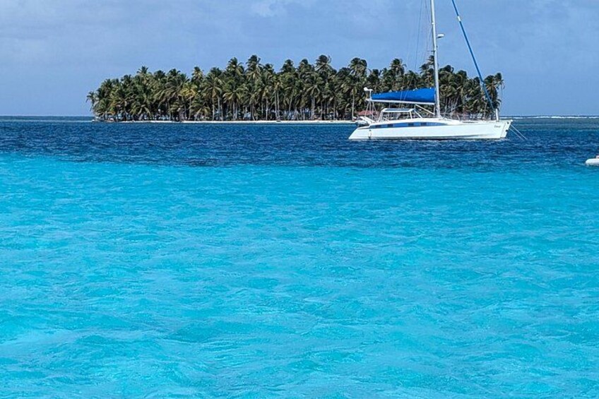 A white sailboat on turquoise water with a small island of palm trees in the background. 1