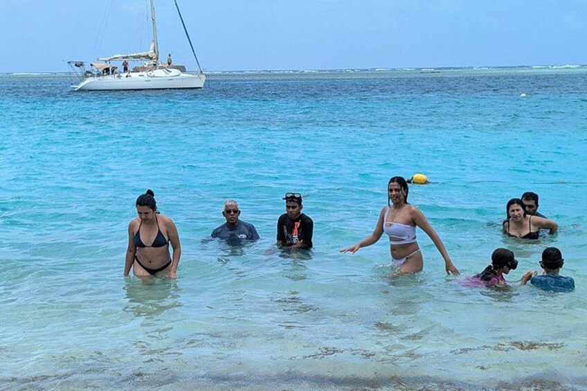 People in shallow water with a sailboat in the background. 5