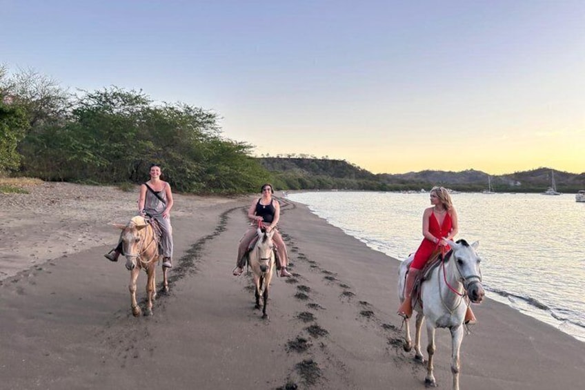 Three people riding horses along a beach path near water. 1