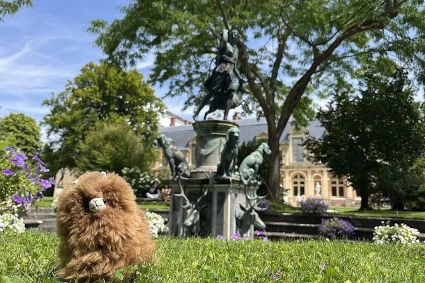 A dog in a park with a statue and a building in the background. 2