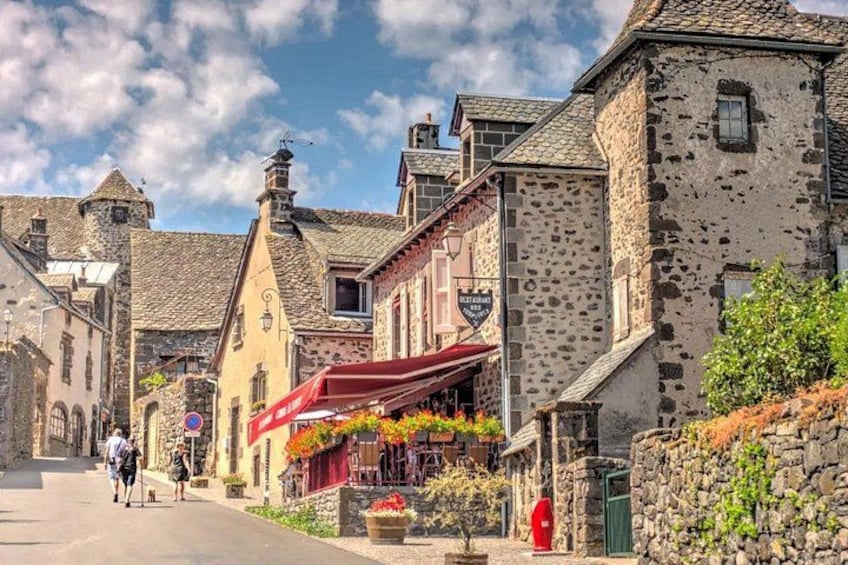 A cobblestone street with historic stone buildings, a red awning, and a flower bed. 3
