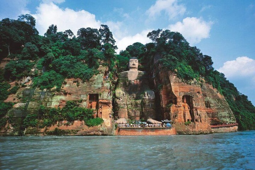 Eine große Buddha-Statue auf einem Felsen, umgeben von üppiger Vegetation und einem Fluss darunter. 3