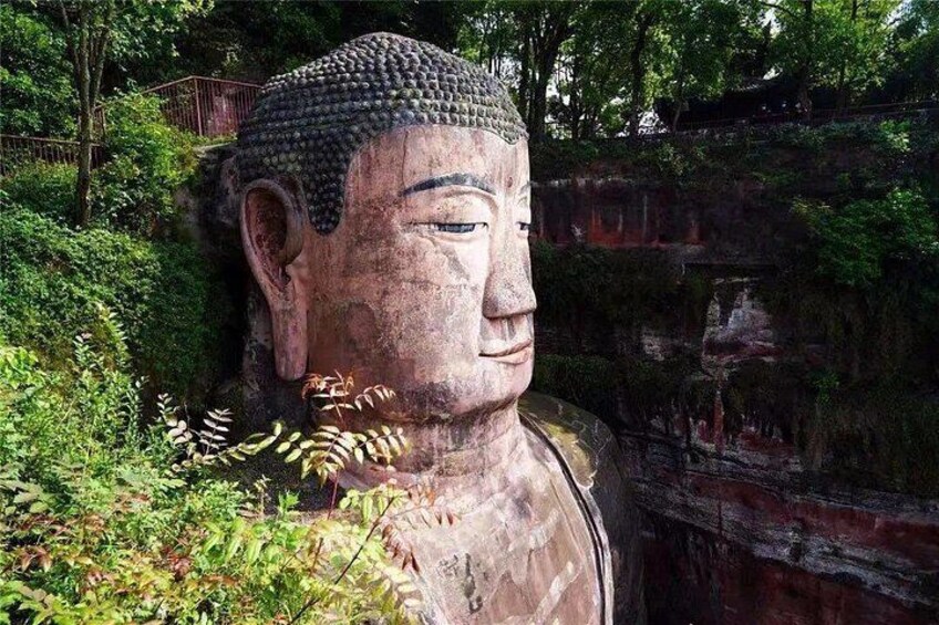 Eine große Buddha-Statue, umgeben von viel Grün und einer felsigen Klippe. 4