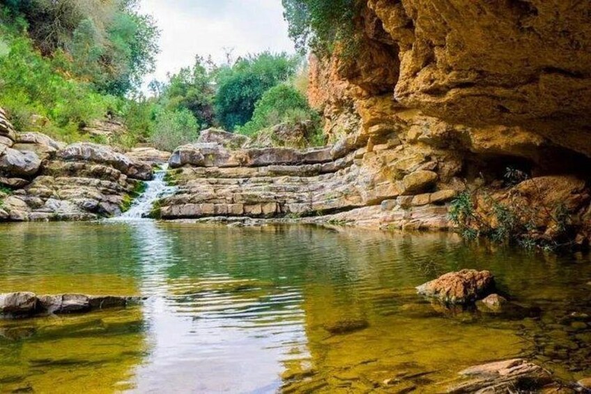 A natural landscape with a waterfall, clear water, and rocky terrain. 2