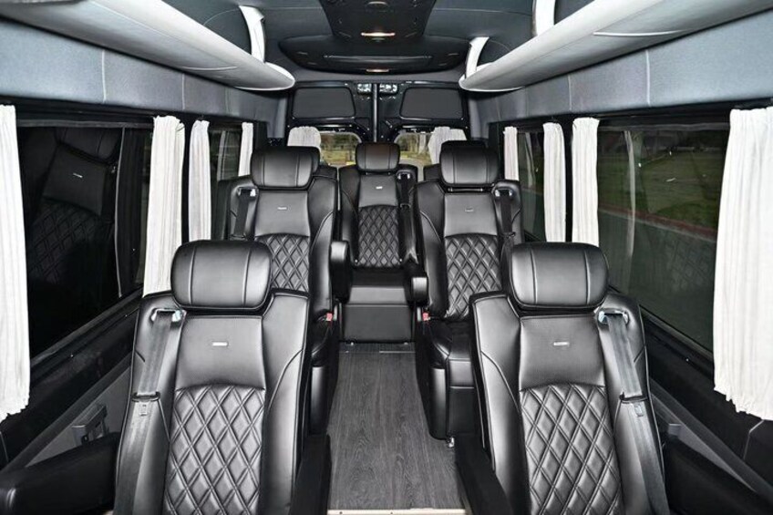 A train interior with black leather seats, white curtains, and a central aisle. 3