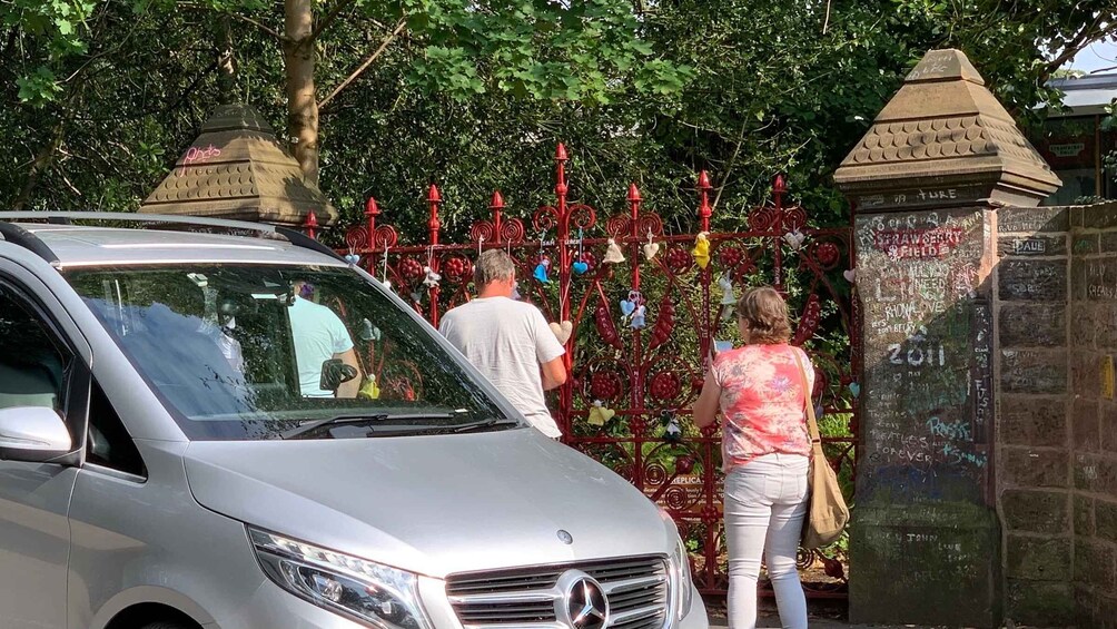 A silver car parked in front of a red metal fence with heart-shaped decorations and a stone wall with graffiti. 3