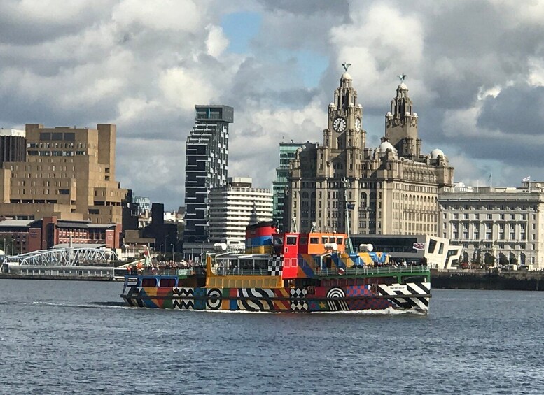 A colorful boat with a unique design on the water, a bridge, and a city skyline with historic buildings in the background. 1
