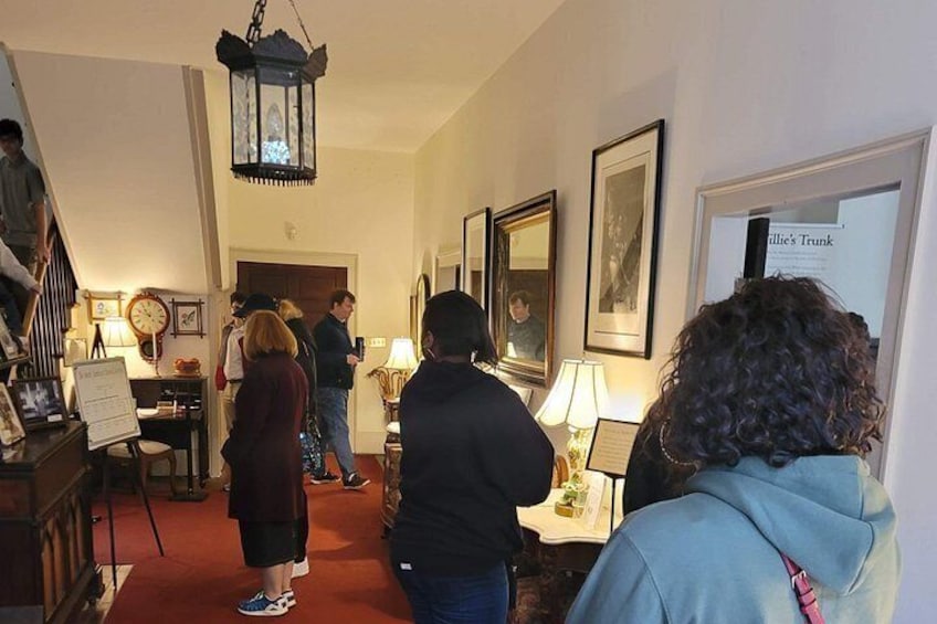 A hallway with people, a staircase, a table with a lamp, and framed pictures on the wall. 2