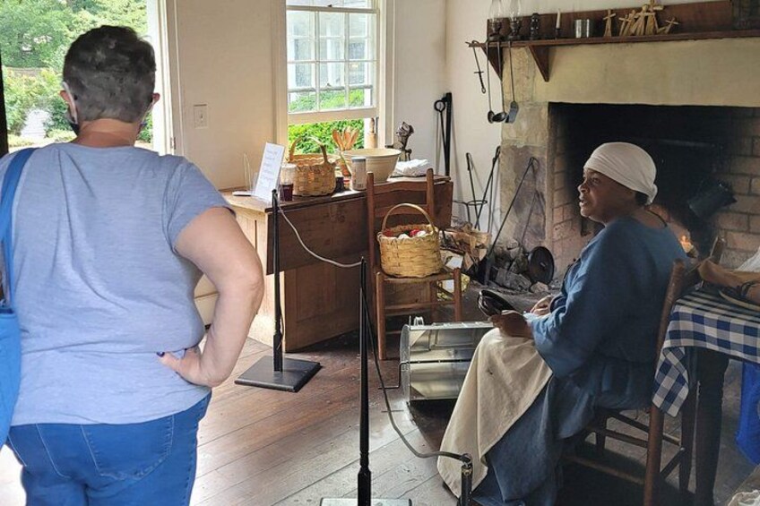 A person standing in a room with a fireplace, a wooden table, and a window. 1