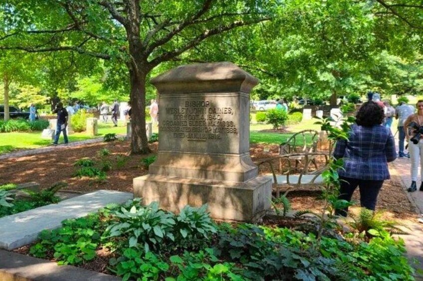 A stone monument with inscriptions, surrounded by greenery and a pathway. 3