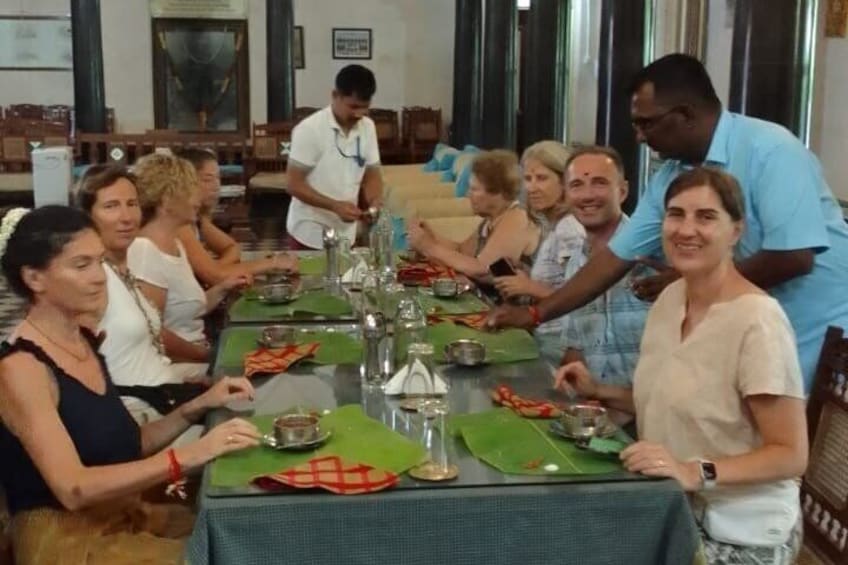 A group of people seated around a table with green placemats, silverware, and glasses, in a room with wooden furniture and a large window. 2