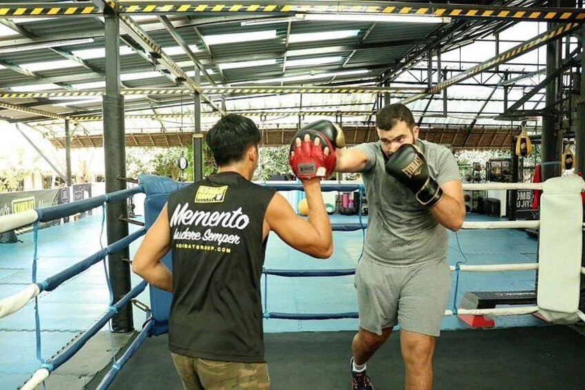 A boxing ring with two individuals training, one wearing a black shirt with 'Memento' text and the other in grey shorts. 5