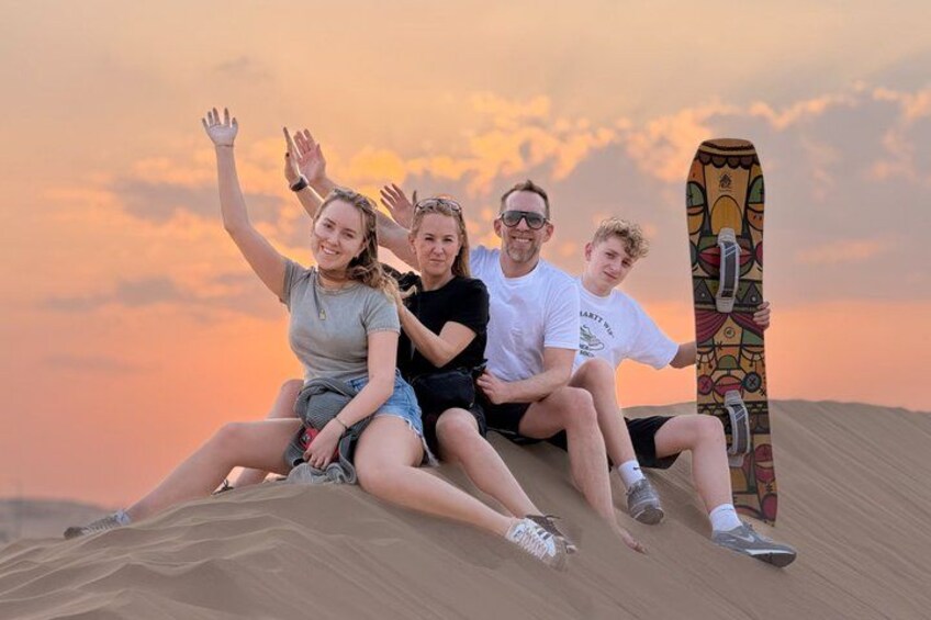 Fire personer sidder på en sanddune med et farverigt skateboard. 2