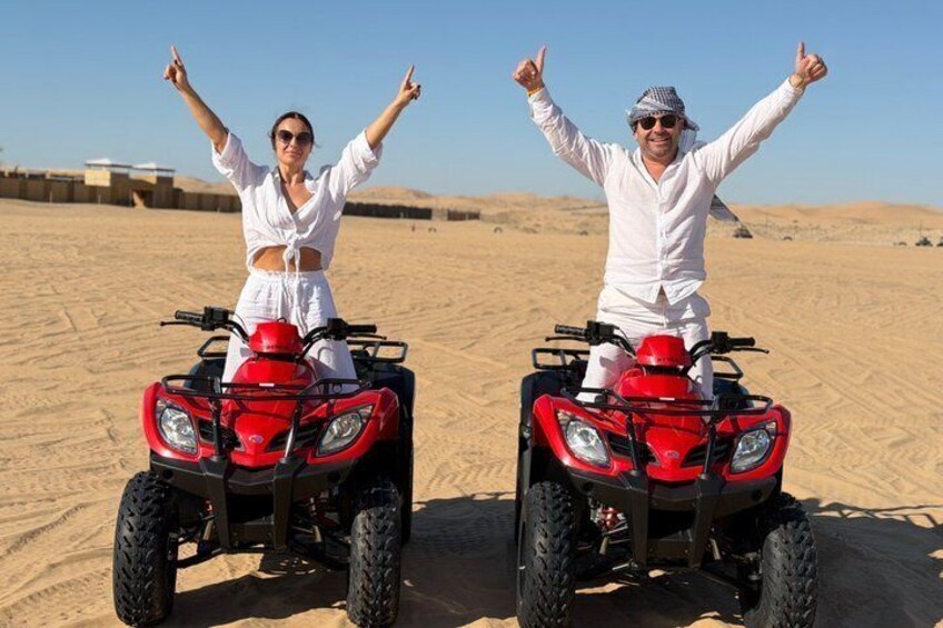 Two people on red ATVs in a desert with sand dunes in the background. 1