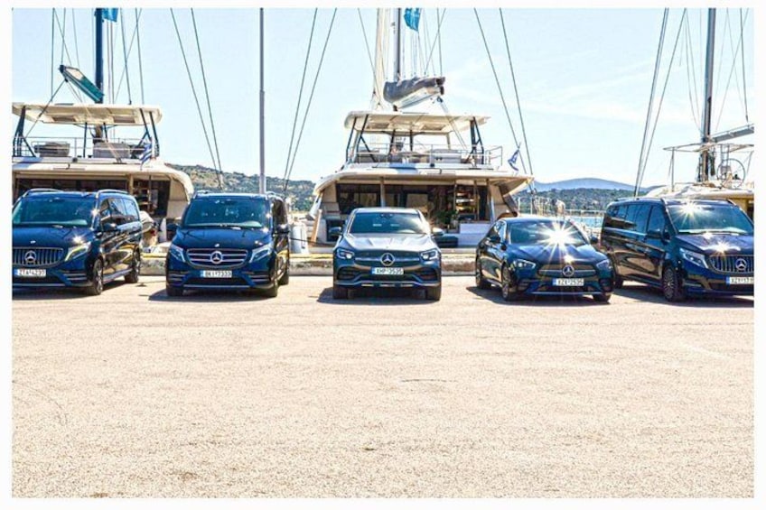 Cinco automóviles Mercedes-Benz estacionados frente a un puerto deportivo con yates y embarcaciones al fondo. 3