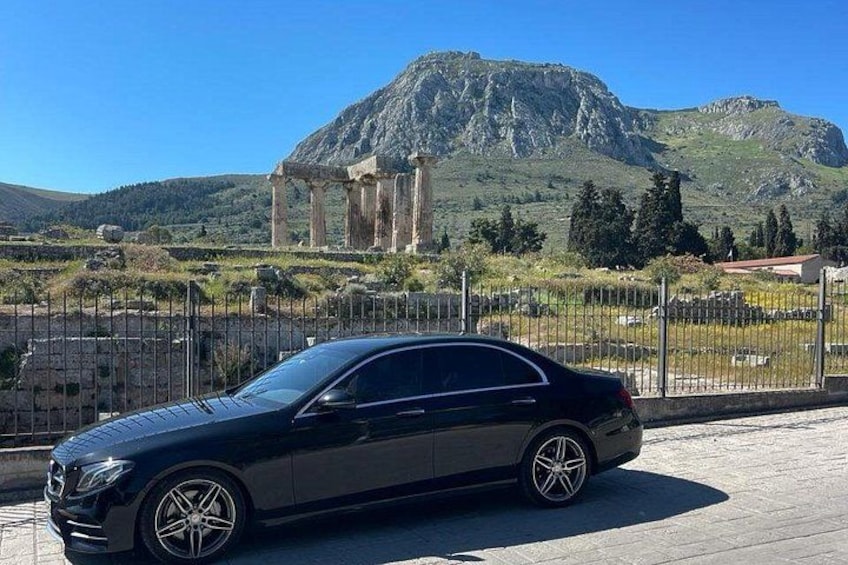 Un coche negro estacionado frente a ruinas antiguas con una montaña al fondo. 1