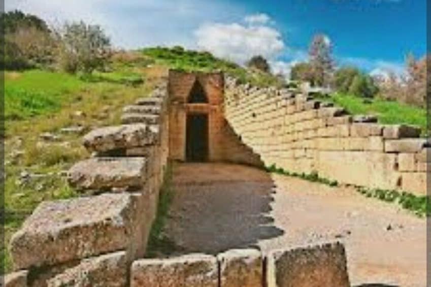 Un sendero de piedra conduce a una estructura con entrada abovedada, rodeada de muros de piedra y vegetación. 2