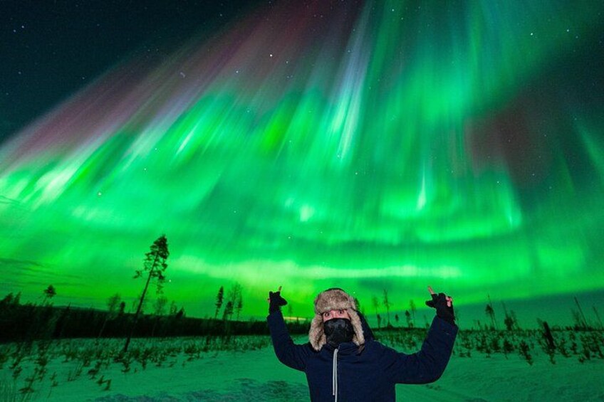 Een persoon staat in een besneeuwd landschap onder een nachthemel met groen poollicht. 1