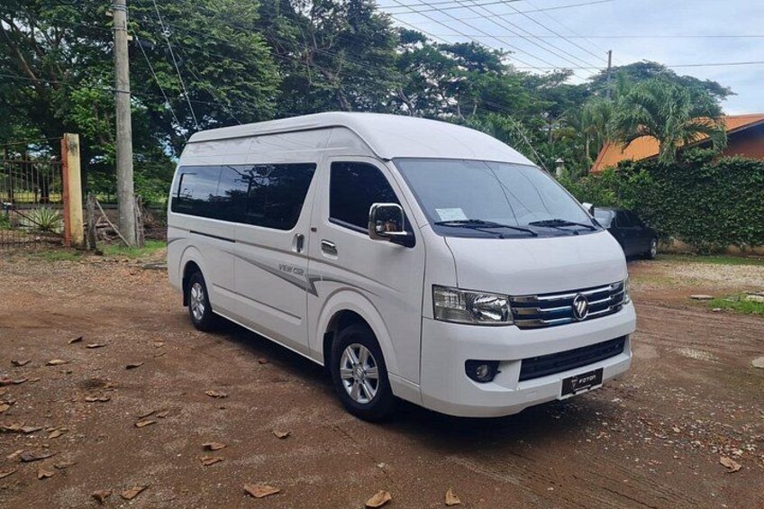 A white van parked on a dirt road with trees and a fence in the background. 2