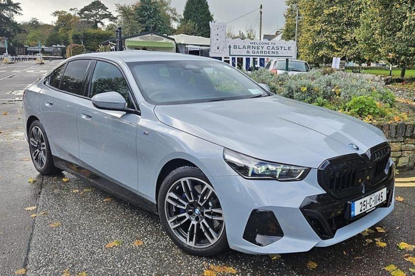 A silver BMW parked in front of a sign that reads 'Welcome to Blarney Castle & Gardens.' 1