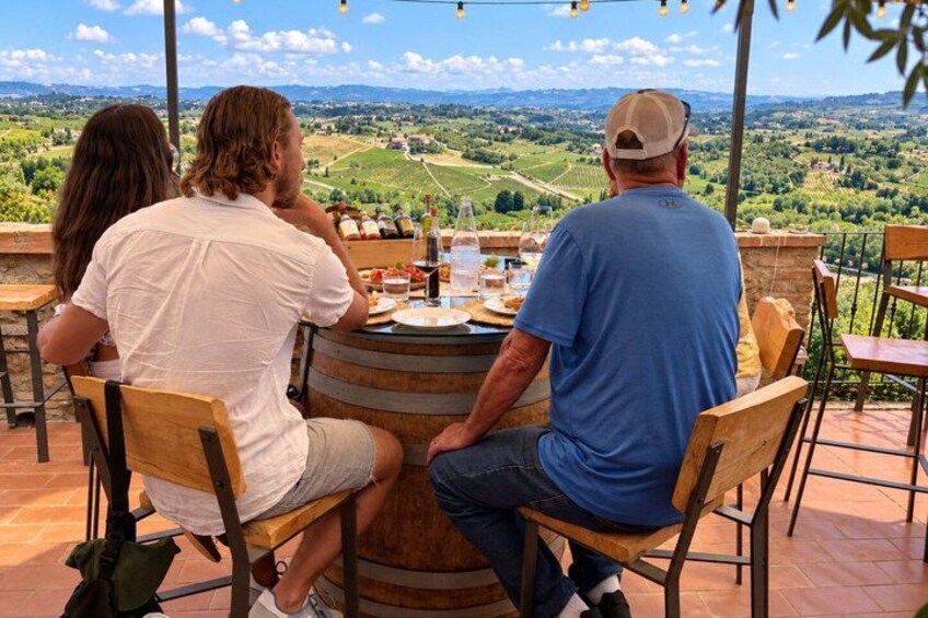 Three people dining at a wooden table with a wine bottle and glasses, overlooking a vineyard. 5