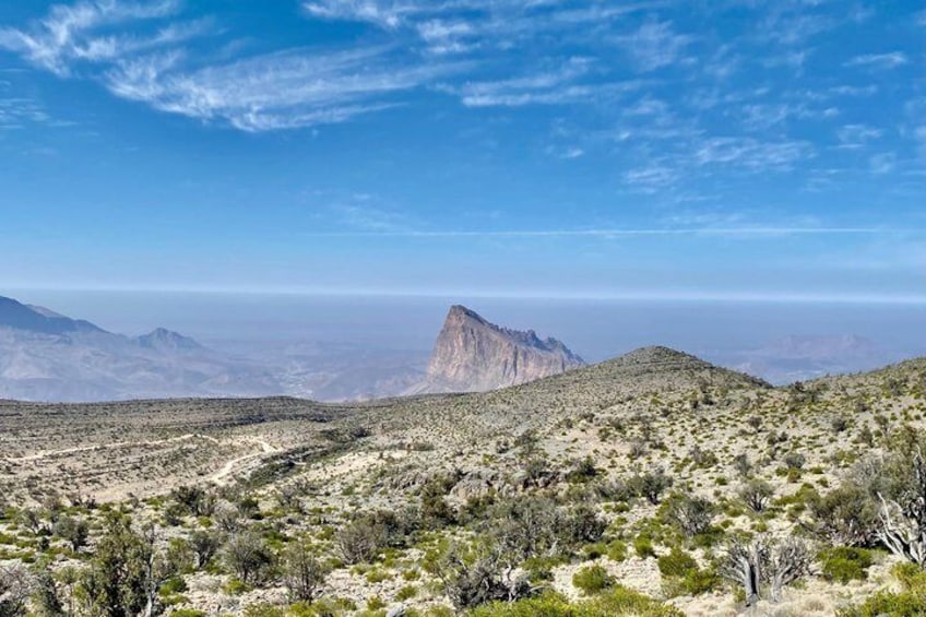 Een woestijnlandschap met schaarse begroeiing, een opvallende bergtop en een helderblauwe lucht. 4